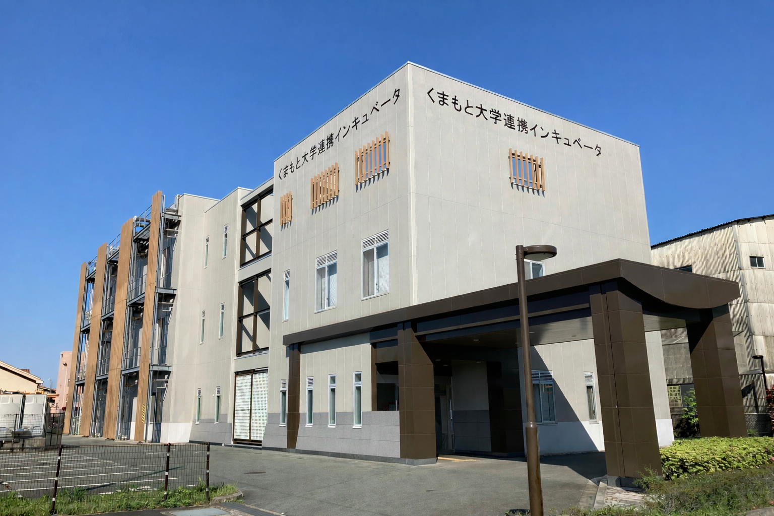 Modern gray university building with wooden slats on the facade and a dark brown entrance canopy under a clear blue sky