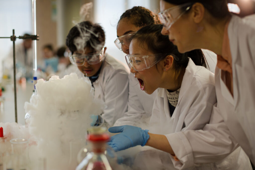 Female teacher and students watching scientific experiment chemical reaction in laboratory classroom - Semicon.TODAY