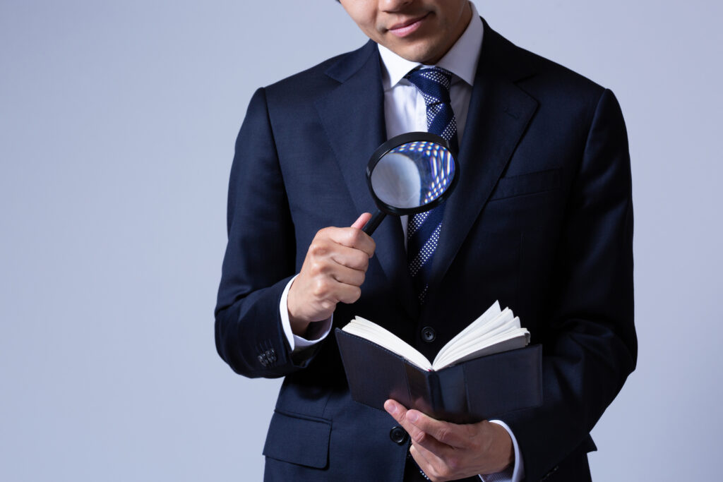 虫眼鏡で手帳を見る男性ビジネスマン - Semicon.TODAY