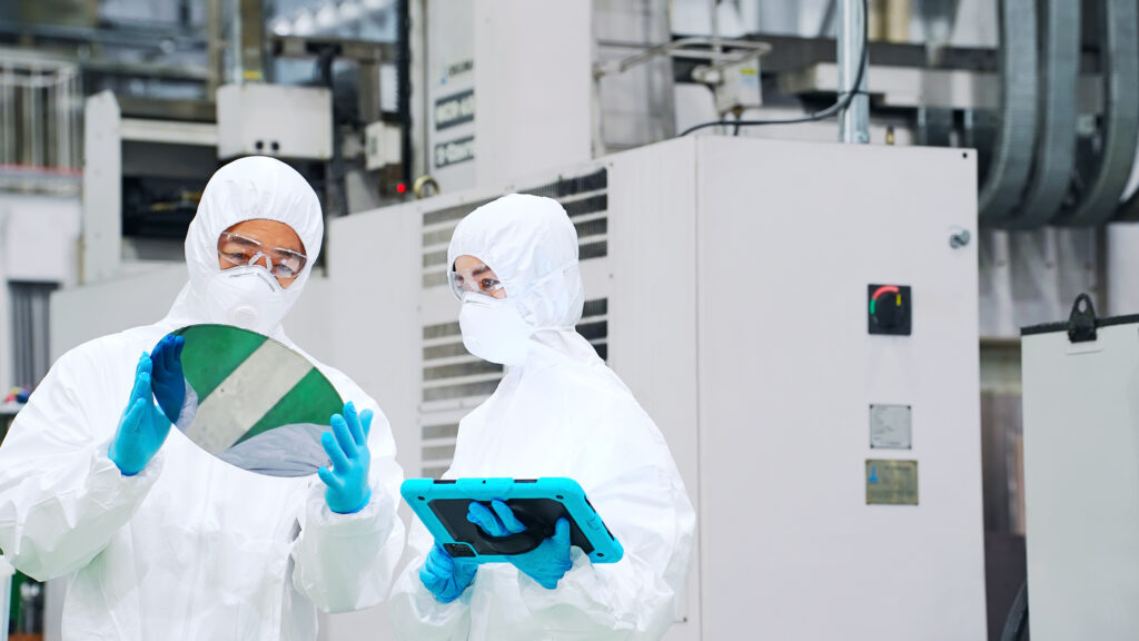 半導体工場でタブレットを持ってシリコンウエハーを検査する防護服を着た男女作業員 - SEMICON.TODAY