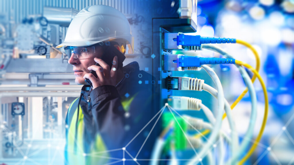 Industrial engineer in helmet communicates by phone near network cables coordinating factory automation and digital connectivity solutions - SEMICON.TODAY