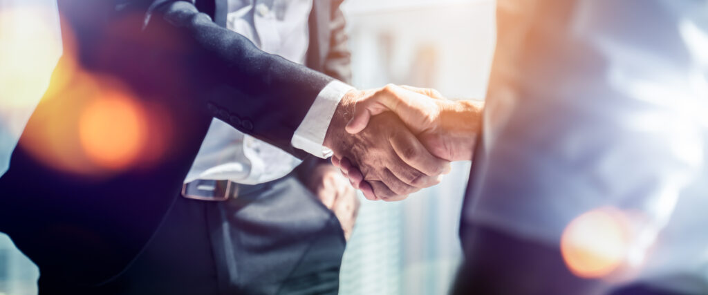 Two professionals shake hands in a business setting, symbolizing an agreement or partnership.