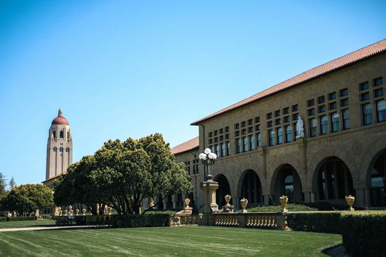 image - SEMICON.TODAY University campus quad with a tall domed tower on the left, a brick arched building, and a green lawn under a blue sky.