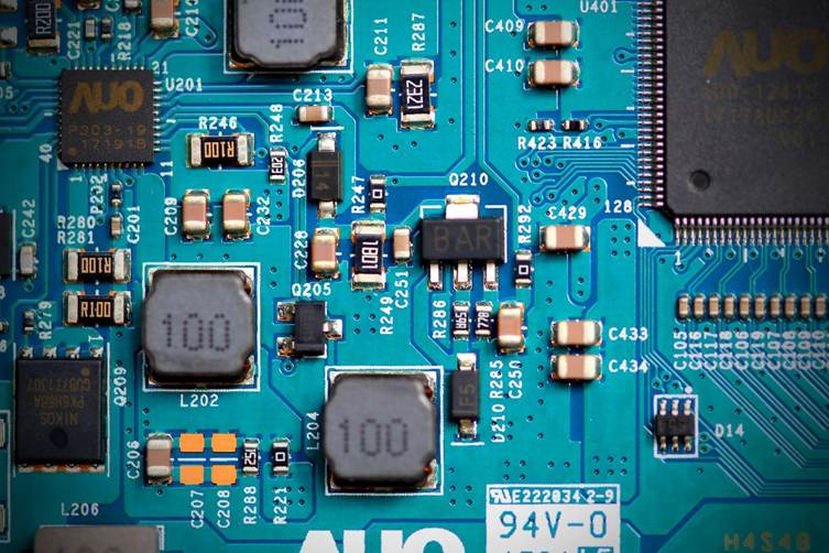 Close-up of a blue computer motherboard with surface-mount components, including two large inductors marked 100 and numerous resistors and capacitors.