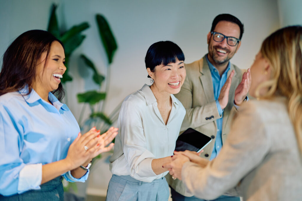 Group of diverse colleagues in an office celebrate, smiling and clapping together.