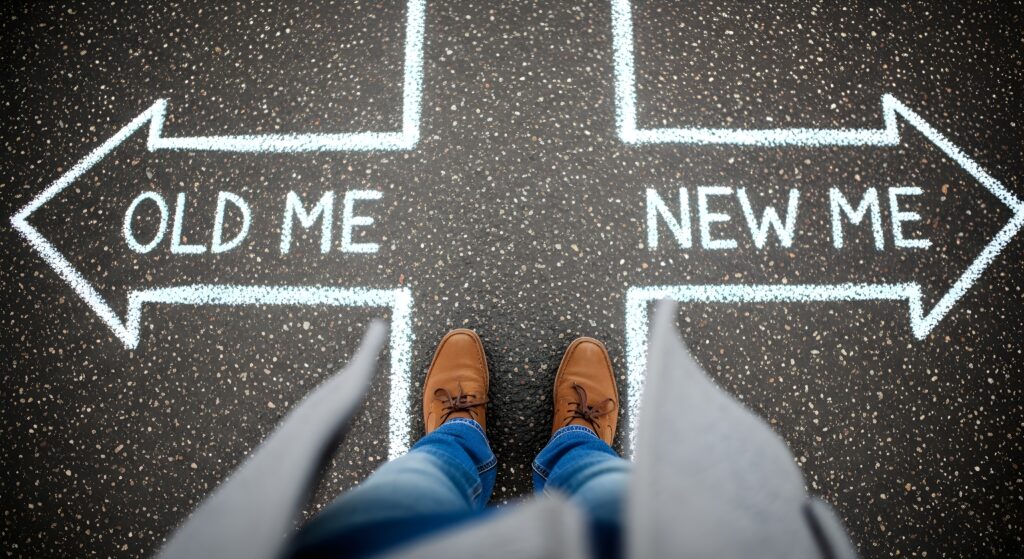 Choosing a New Direction Person Standing at Crossroads Between Old and New Self - SEMICON.TODAY Feet in brown shoes stand on a pavement with arrows and the phrases 'OLD ME' and 'NEW ME' indicating a choice or crossroads.