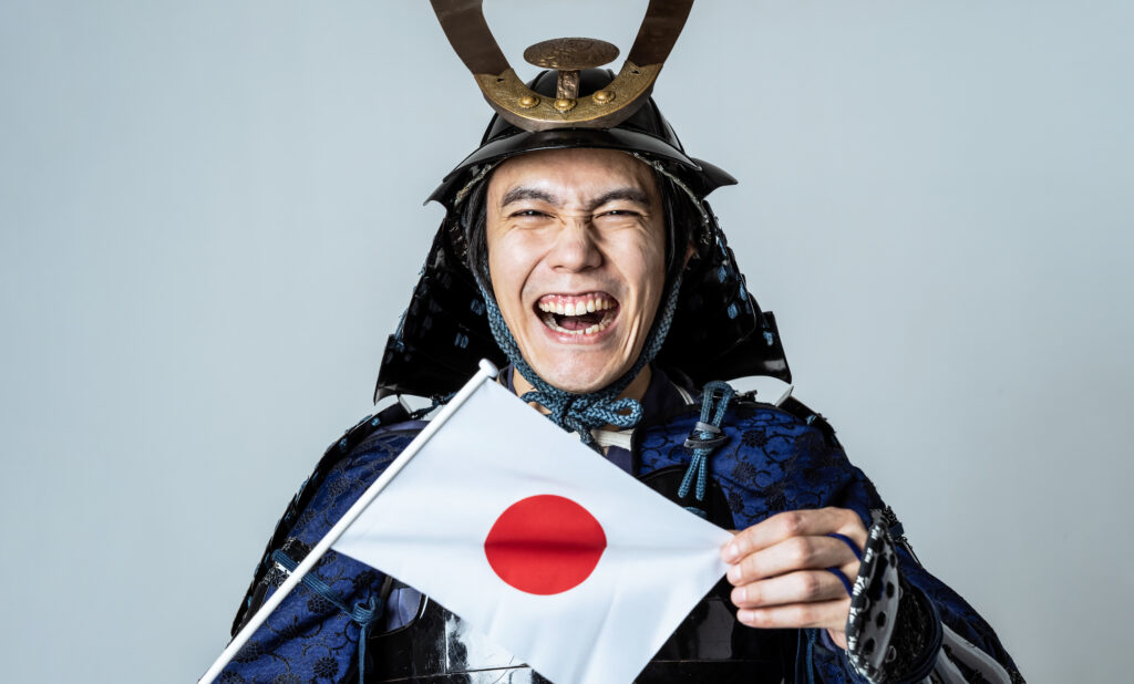 日の丸を掲げるサムライ ニッポンを応援 - SEMICON.TODAY Person in traditional samurai armor laughing while holding a small Japanese flag.