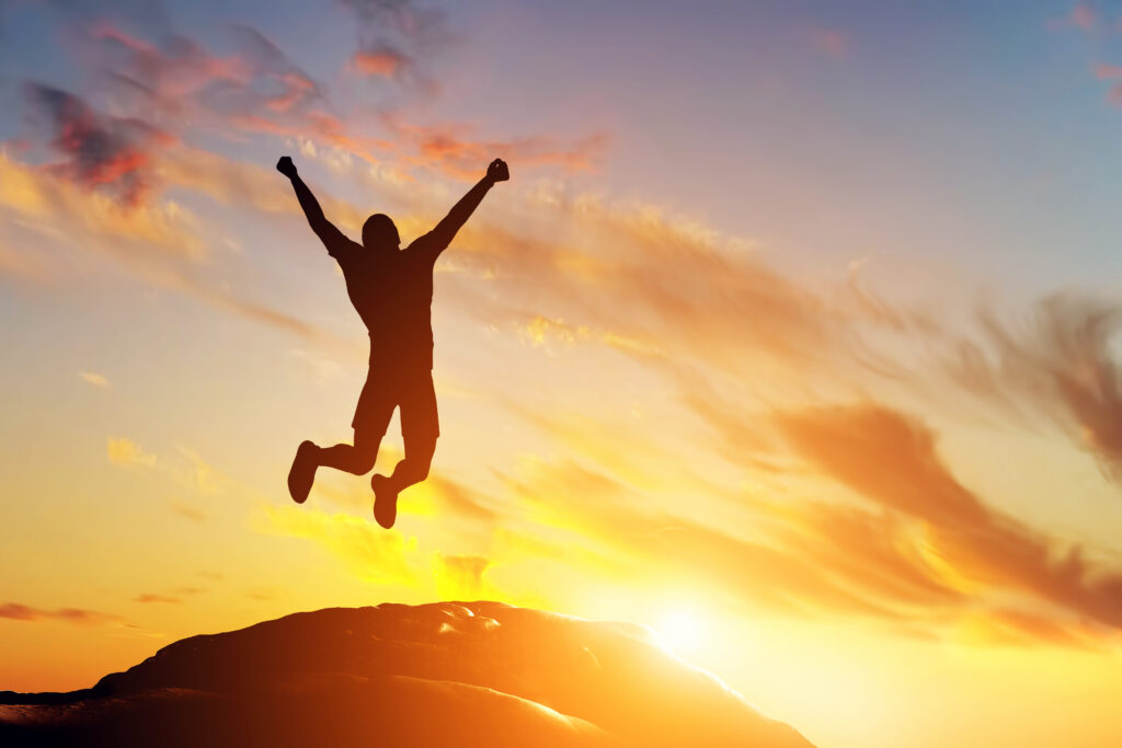 Happy man jumping for joy on the peak of the mountain Success - SEMICON.TODAY Silhouette of a person jumping with arms raised on a hill at sunset with a orange-pink sky