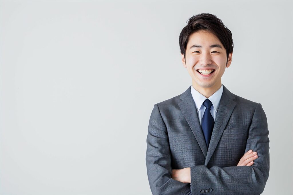 Man in a gray suit smiling with arms crossed against a light background.