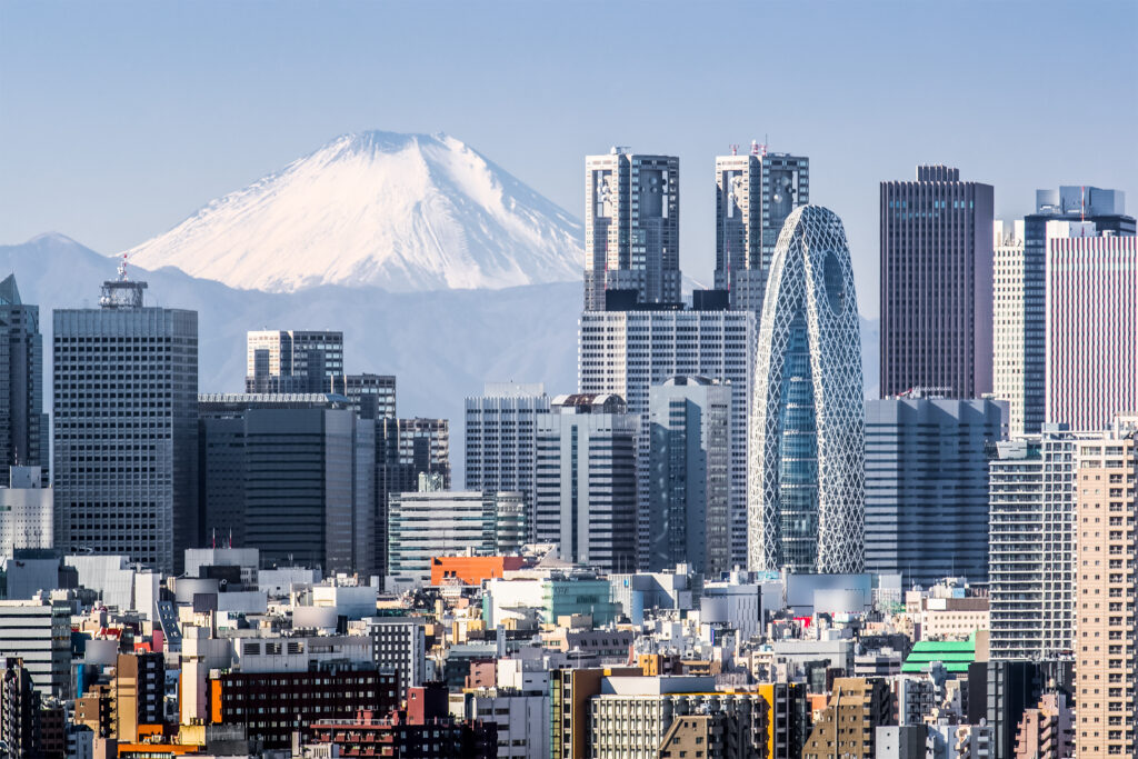 Snow-capped Mount Fuji rises behind Tokyo's modern skyline with numerous high-rise buildings in the foreground on a clear day.