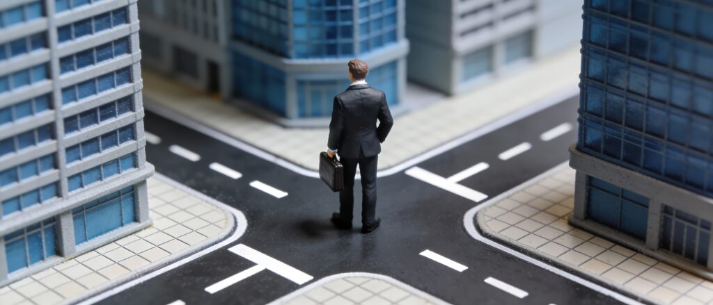 Miniature businessman in a dark suit holding a briefcase, standing at a model city intersection.