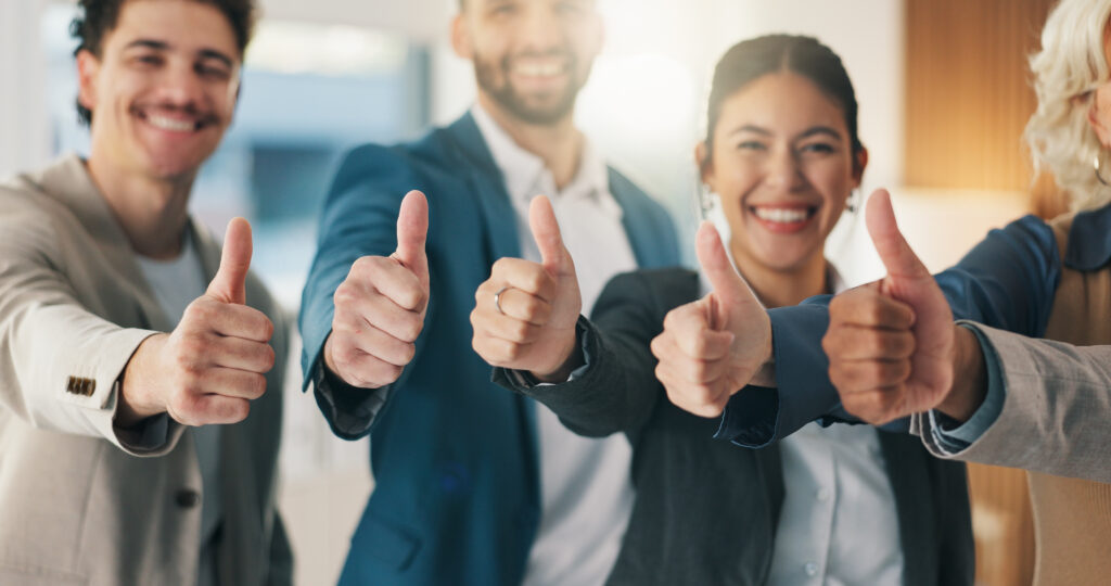 Four coworkers giving thumbs up in a bright office, smiling and celebrating.] ]}