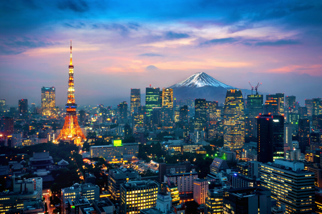 Tokyo skyline at dusk with illuminated skyscrapers and a snow-capped Mount Fuji in the distance.