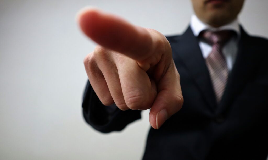指示を出すビジネスマンのクローズアップ - SEMICON.TODAY Close-up of a person in a dark suit pointing directly at the camera, as if giving a command or focus gesture.